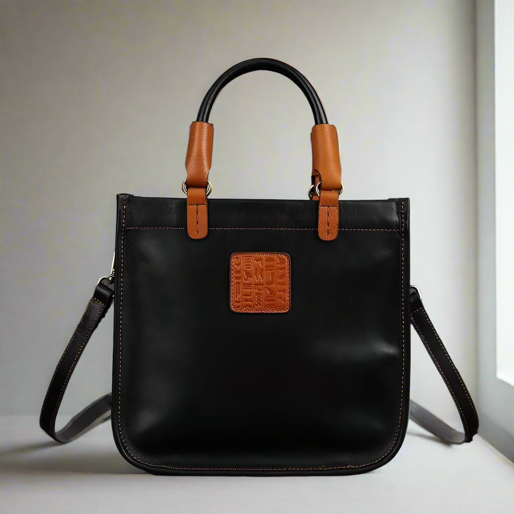 Black handbag with brown leather straps and accents on a white background