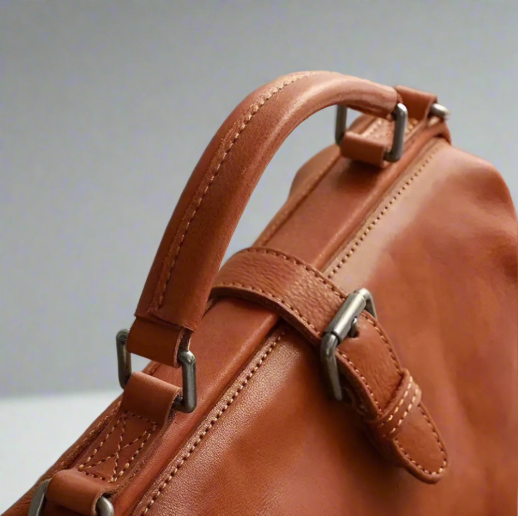 Close-up of a brown leather bag with metal straps against a blurred background