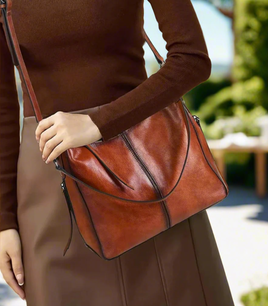 Person holding a brown leather handbag outdoors