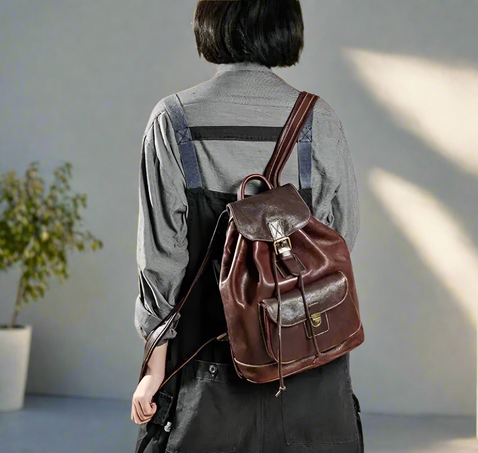 Person wearing a brown leather backpack against a textured wall.