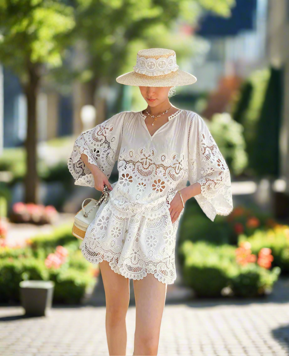 Woman wearing a white lace outfit and hat standing against a backyard garden, sunny