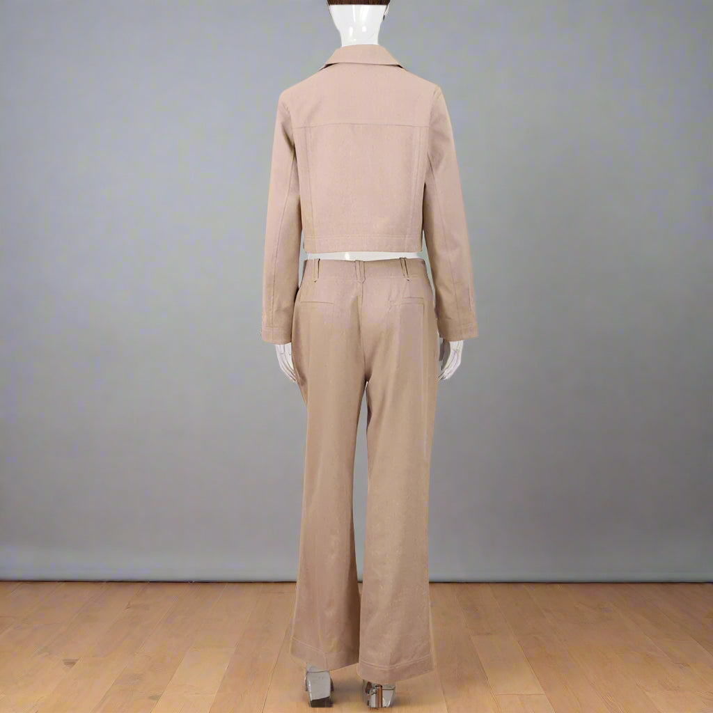 Beige jumpsuit on a mannequin against a white wall with wooden floor