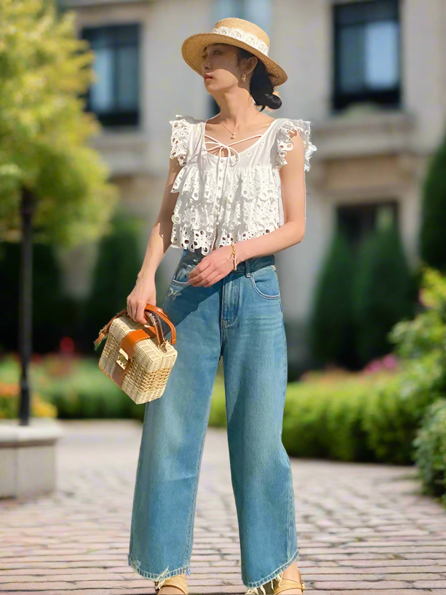 Woman wearing a white top and blue jeans, holding a woven bag, standing in backyard garden, sunny