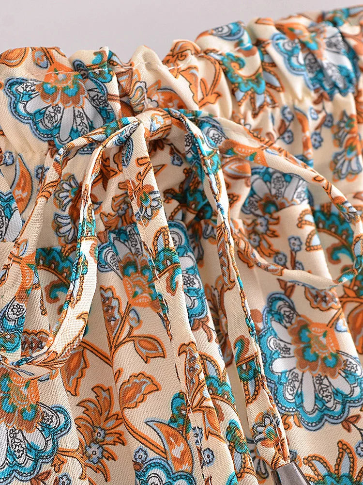 Close-up of a floral patterned fabric with orange and blue accents on a beige background.
