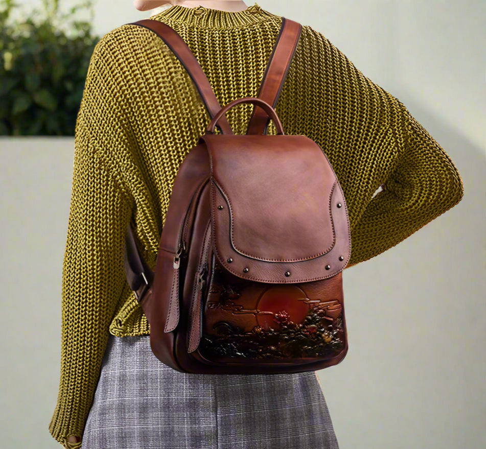 Person wearing a brown leather backpack with a scenic design, wearing a green sweater and plaid skirt.