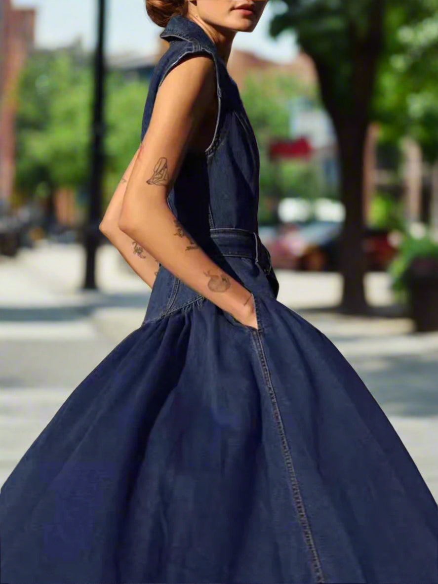 Person wearing a blue denim dress with tattoos on arms, standing against a backyard, sunset