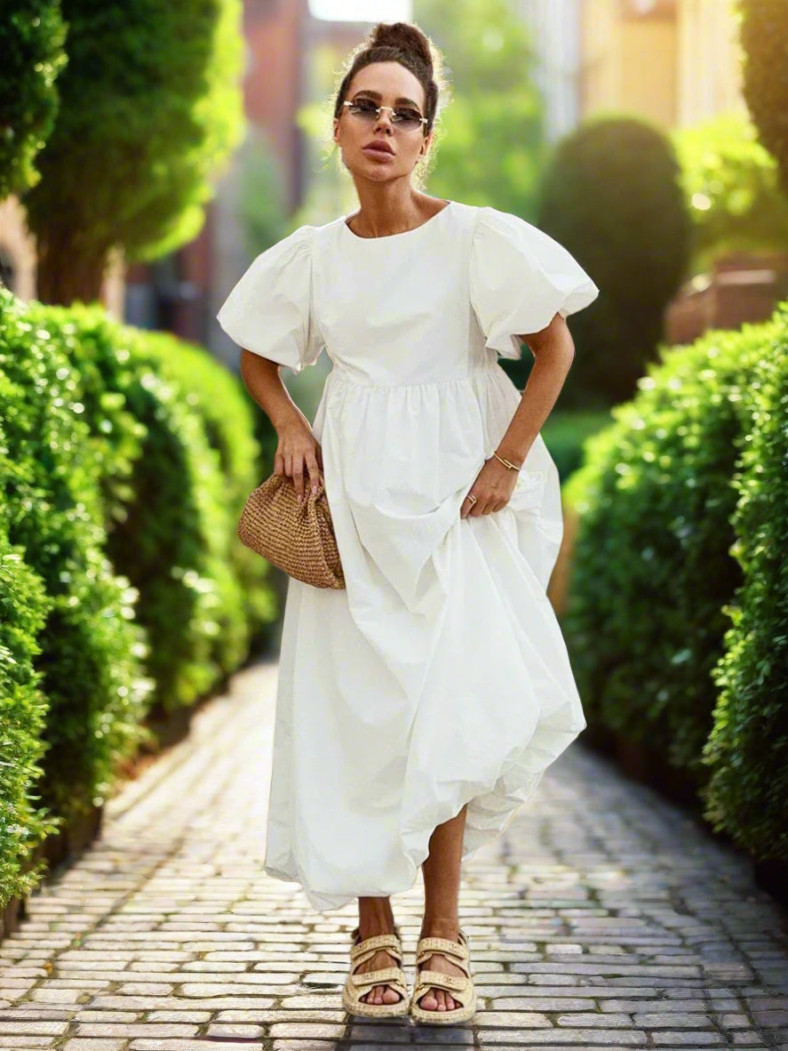 Woman in a white dress standing against a brick wall.