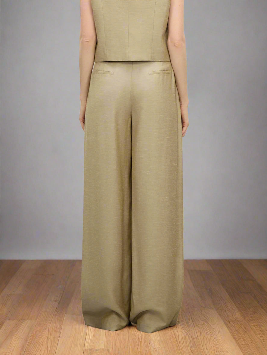 Person wearing a beige sleeveless top and wide-leg pants on a plain background