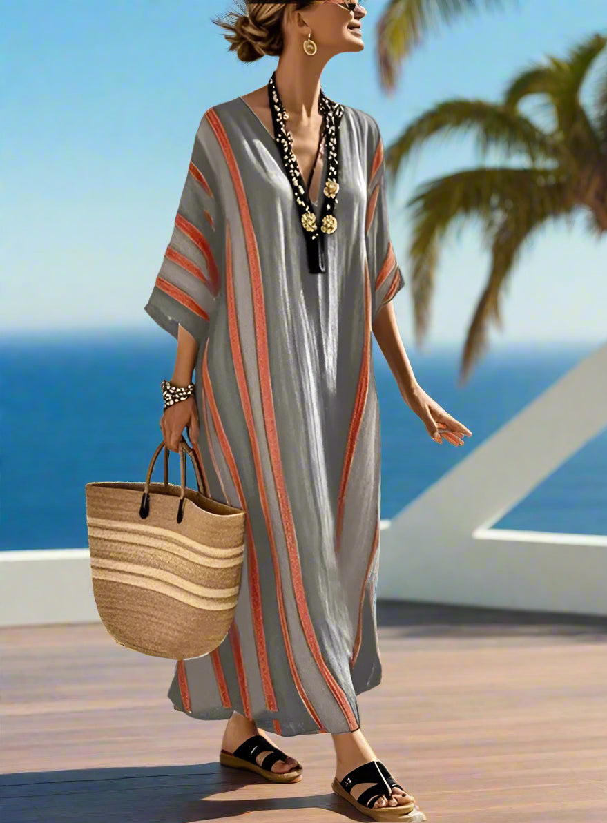 Woman in a striped dress with a woven bag standing on a wooden deck overlooking the ocean.