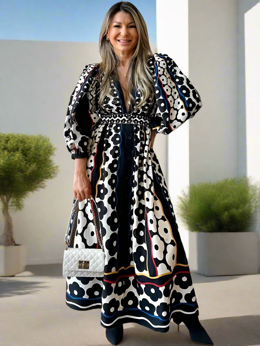 Woman wearing a patterned dress holding a handbag against a brick wall.