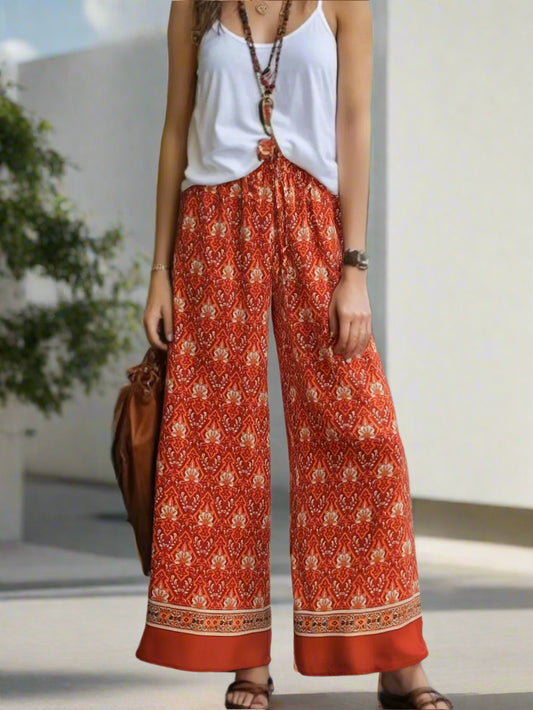Person wearing a white top and red patterned pants with a brown bag, standing outdoors.