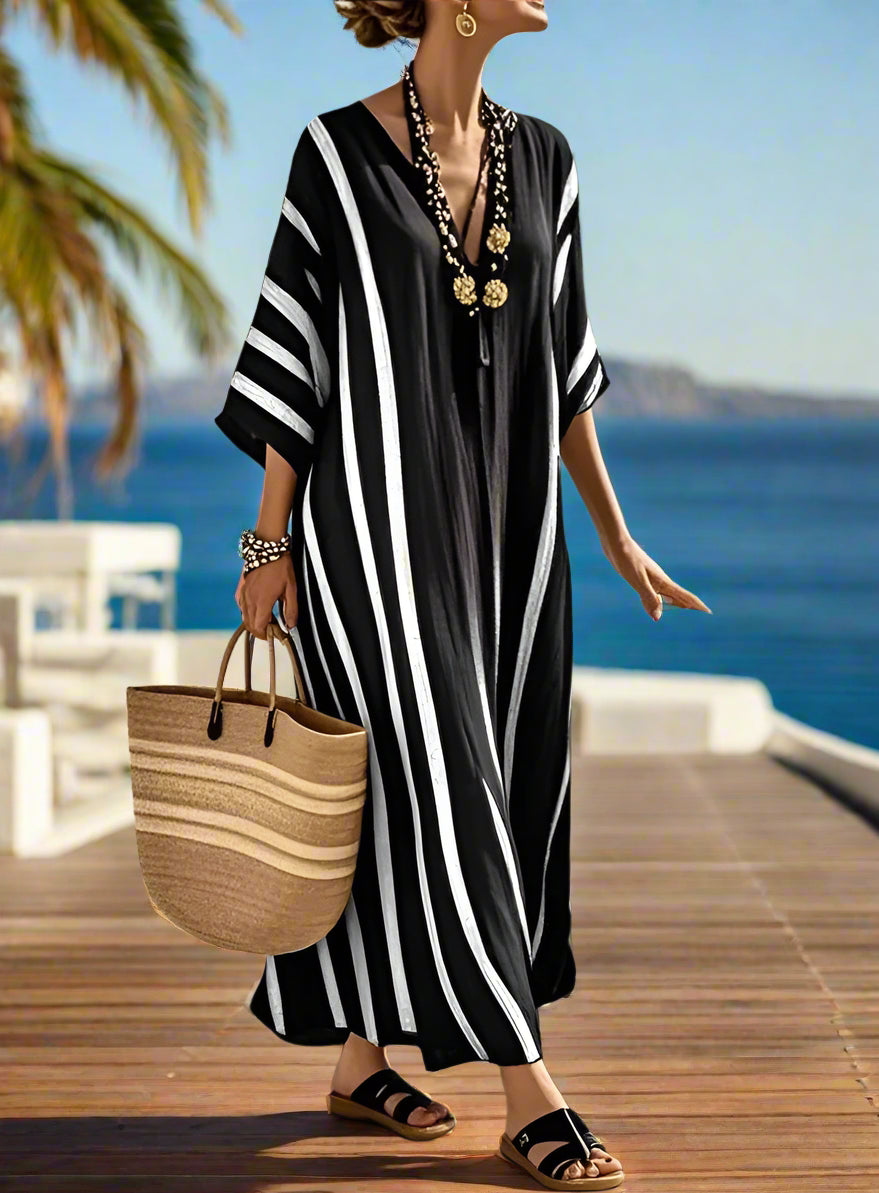 Woman in a black and white striped dress with a straw bag, standing on a wooden deck overlooking the ocean.