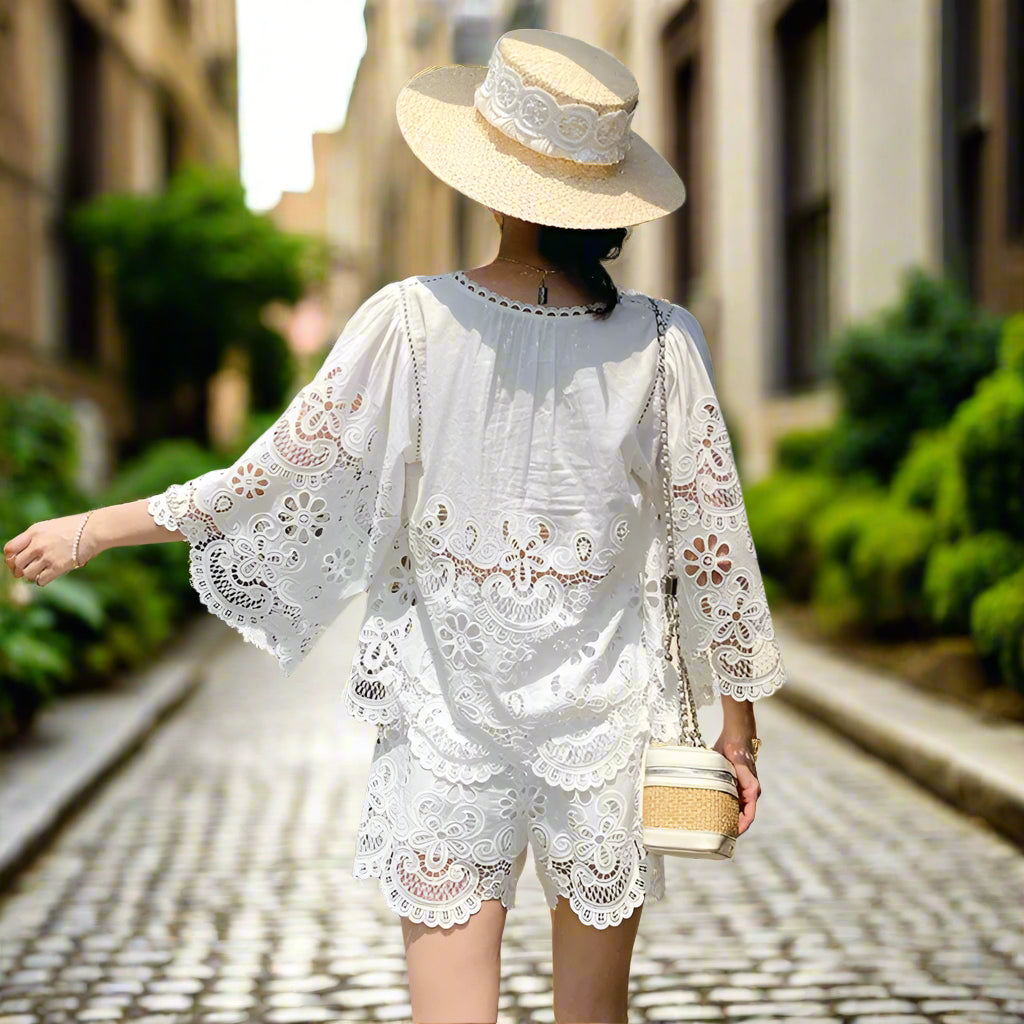 Woman wearing a white lace dress and hat, standing in front of a backyard garden, sunny 