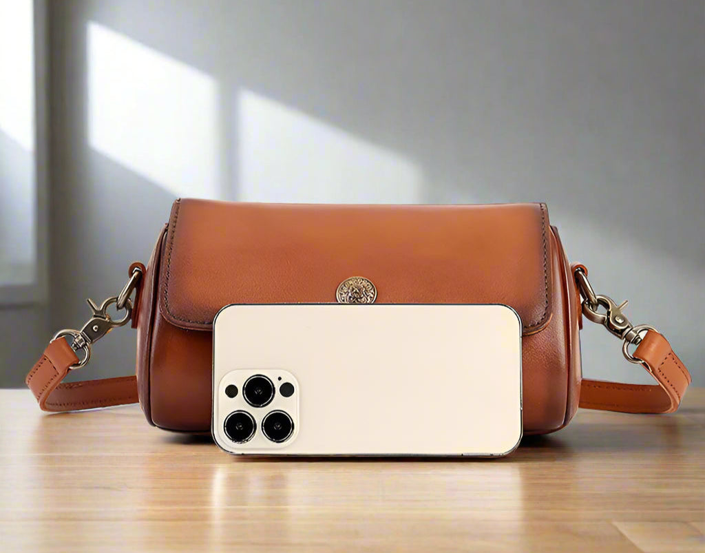 Brown leather handbag with smartphone next to it, showing dimensions on a white background