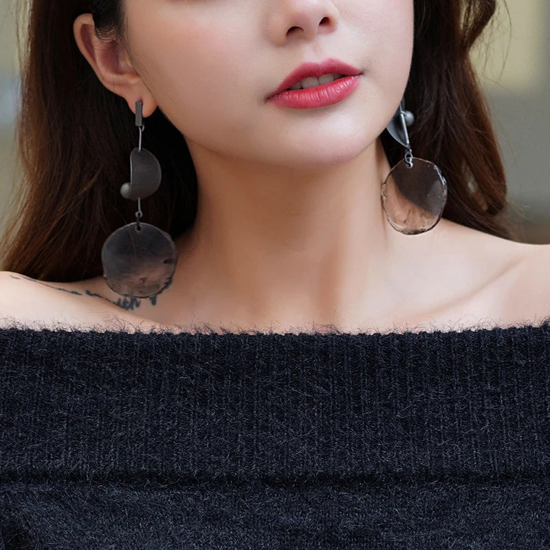 Close-up of a woman wearing large, dangling earrings with a blurred background