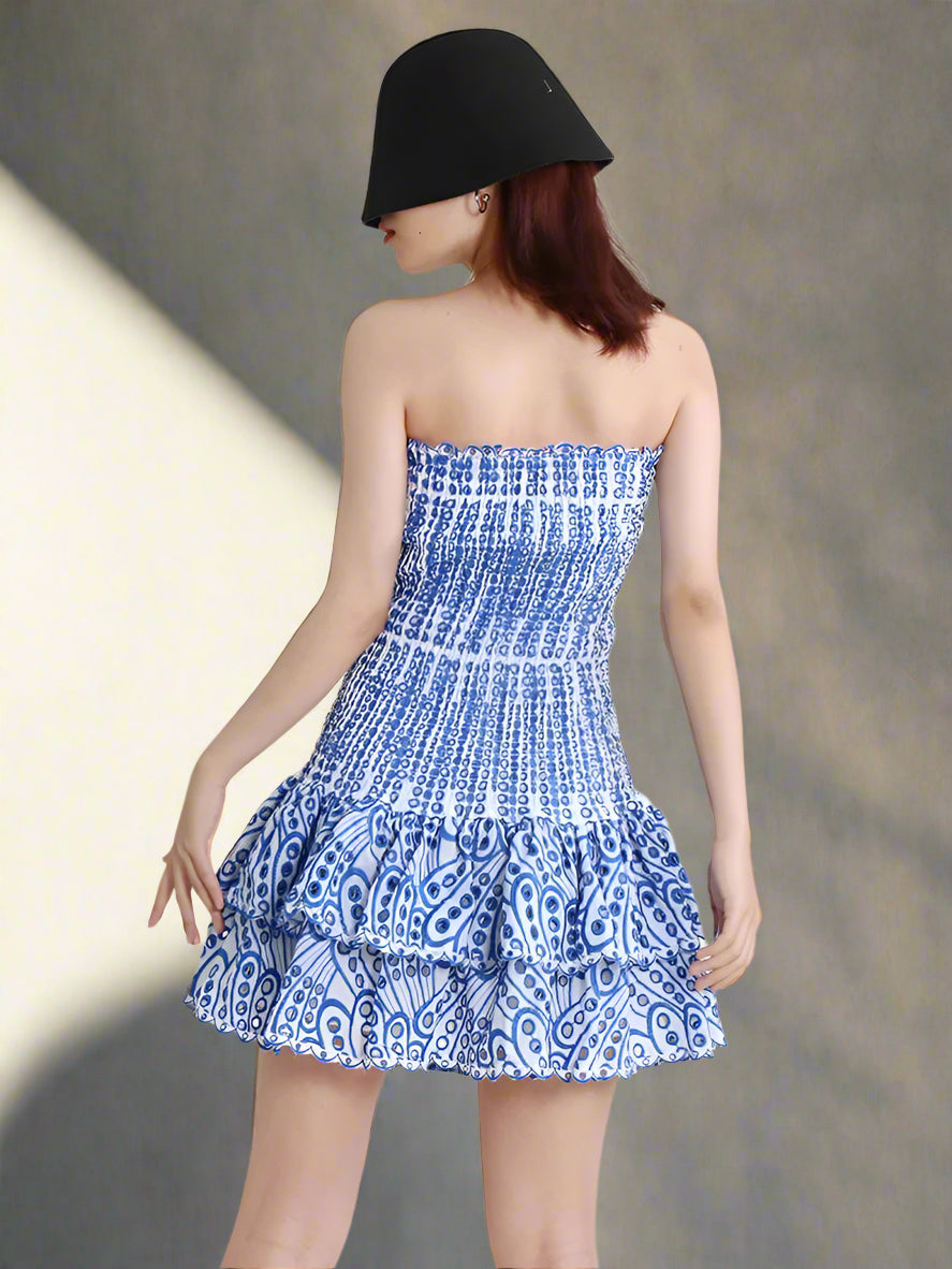 Woman wearing a blue and white patterned strapless dress with a black hat on a backyard, sunny