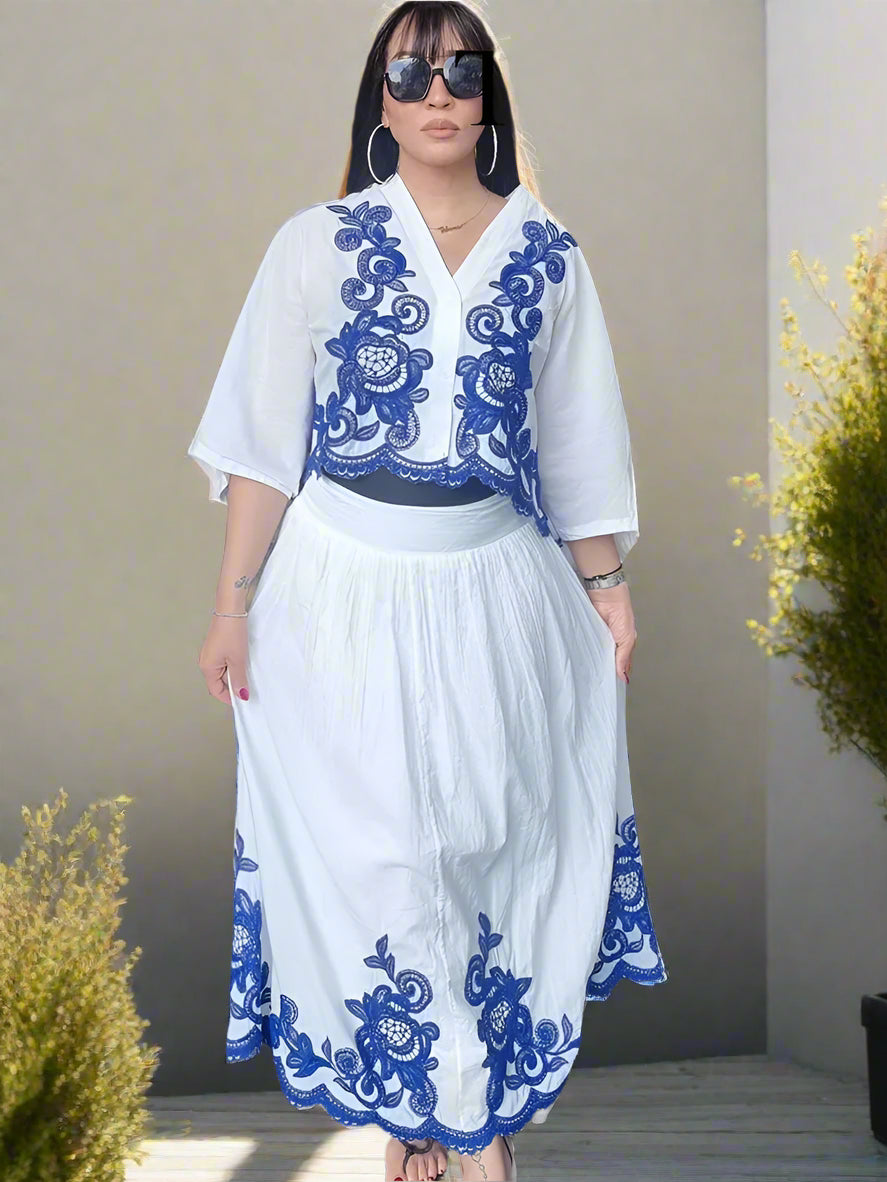 Woman wearing a white outfit set  with blue embroidery , in a backyard garden