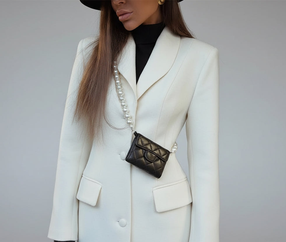 Woman wearing a white coat, black gloves, and a pearl necklace with a black handbag.