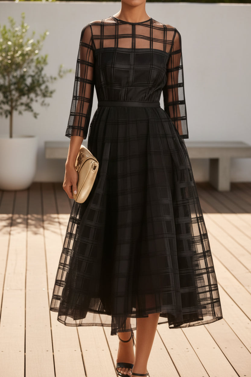 Black dress with sheer sleeves and a gold clutch on a backyard