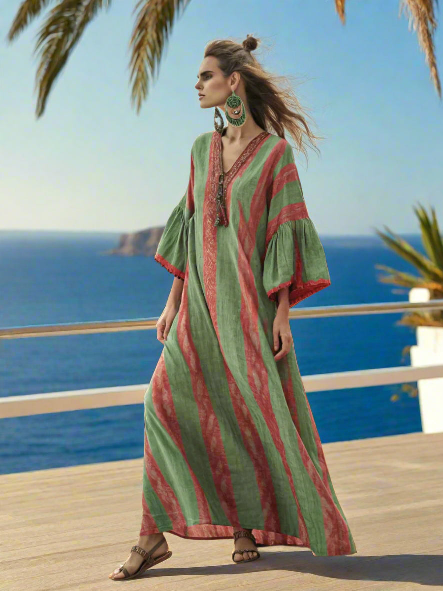 Woman in a green and red striped dress standing on a beach with  water in the background.