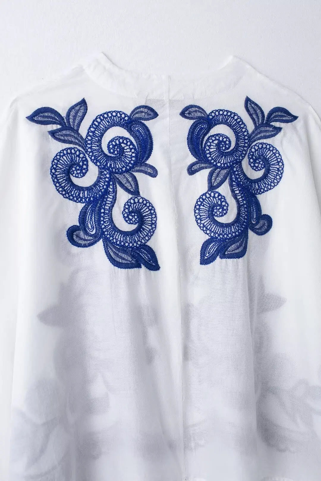 White garment with blue floral embroidery on a white background
