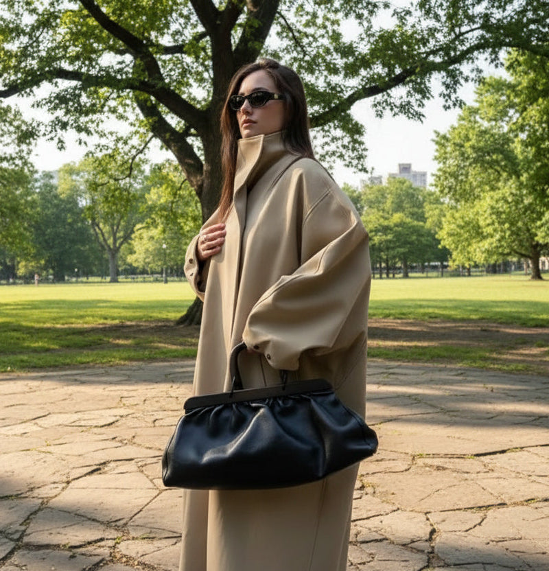 Woman in a beige coat holding a black handbag on a sunny park