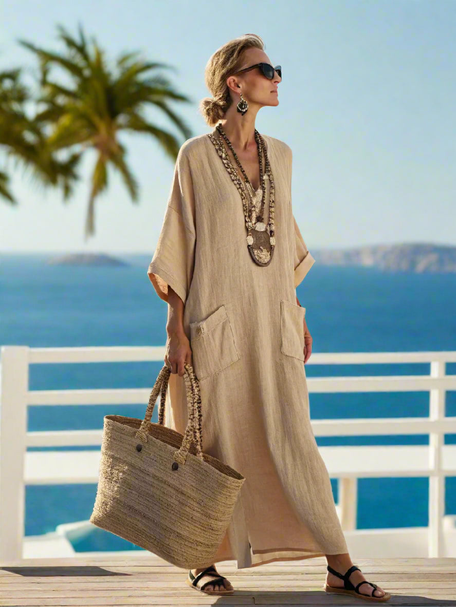 Woman in a beige dress with a large straw bag standing on a scenic coastal path.