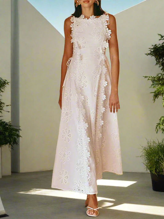Woman wearing a white lace dress standing against a white wall.