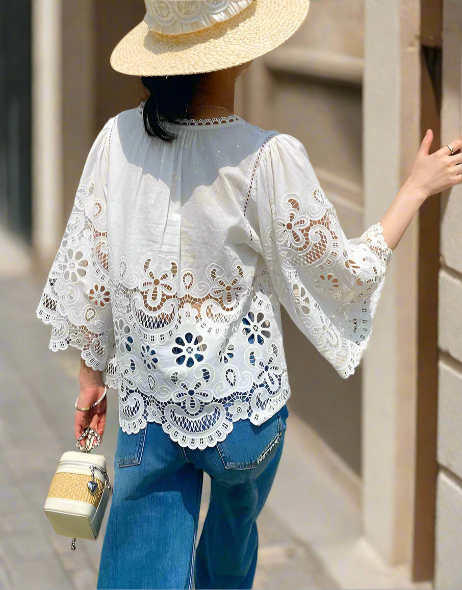 Person wearing a white lace blouse and blue jeans, standing outdoors near a wooden door.