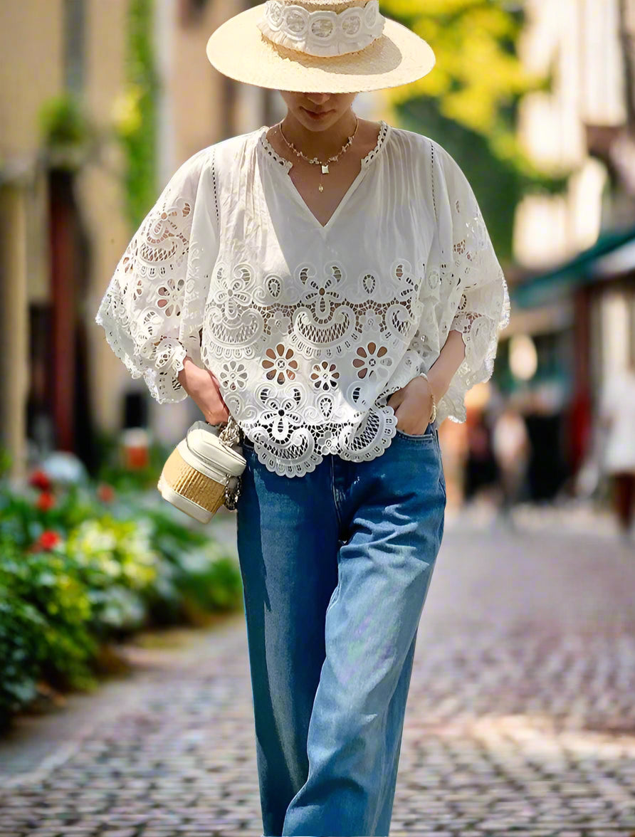 Person wearing a white lace top and blue jeans outdoors.