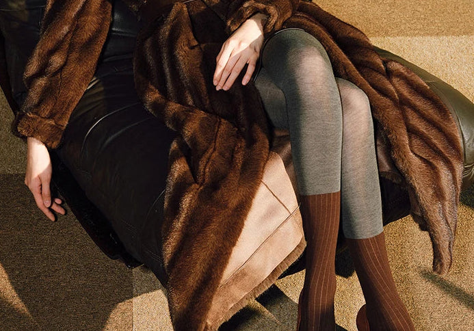 Person wearing a fur coat sitting on a chair indoors.