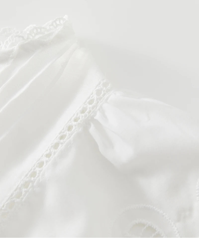 Close-up of a white fabric with lace detailing on a light gray background
