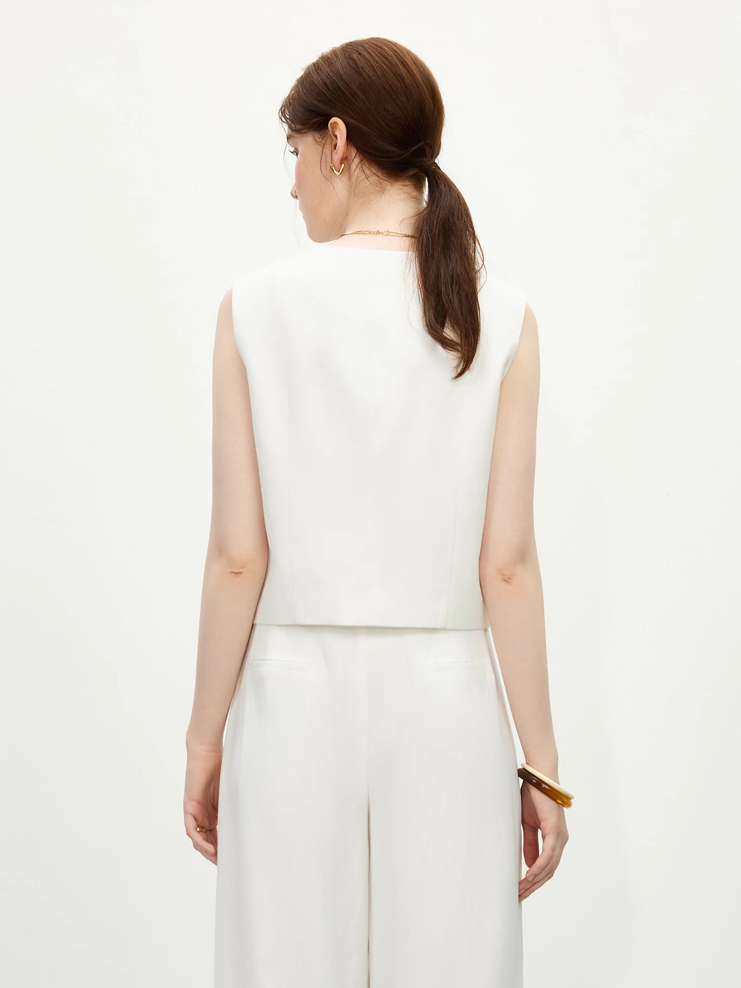 Woman wearing a white sleeveless top and pants on a white background