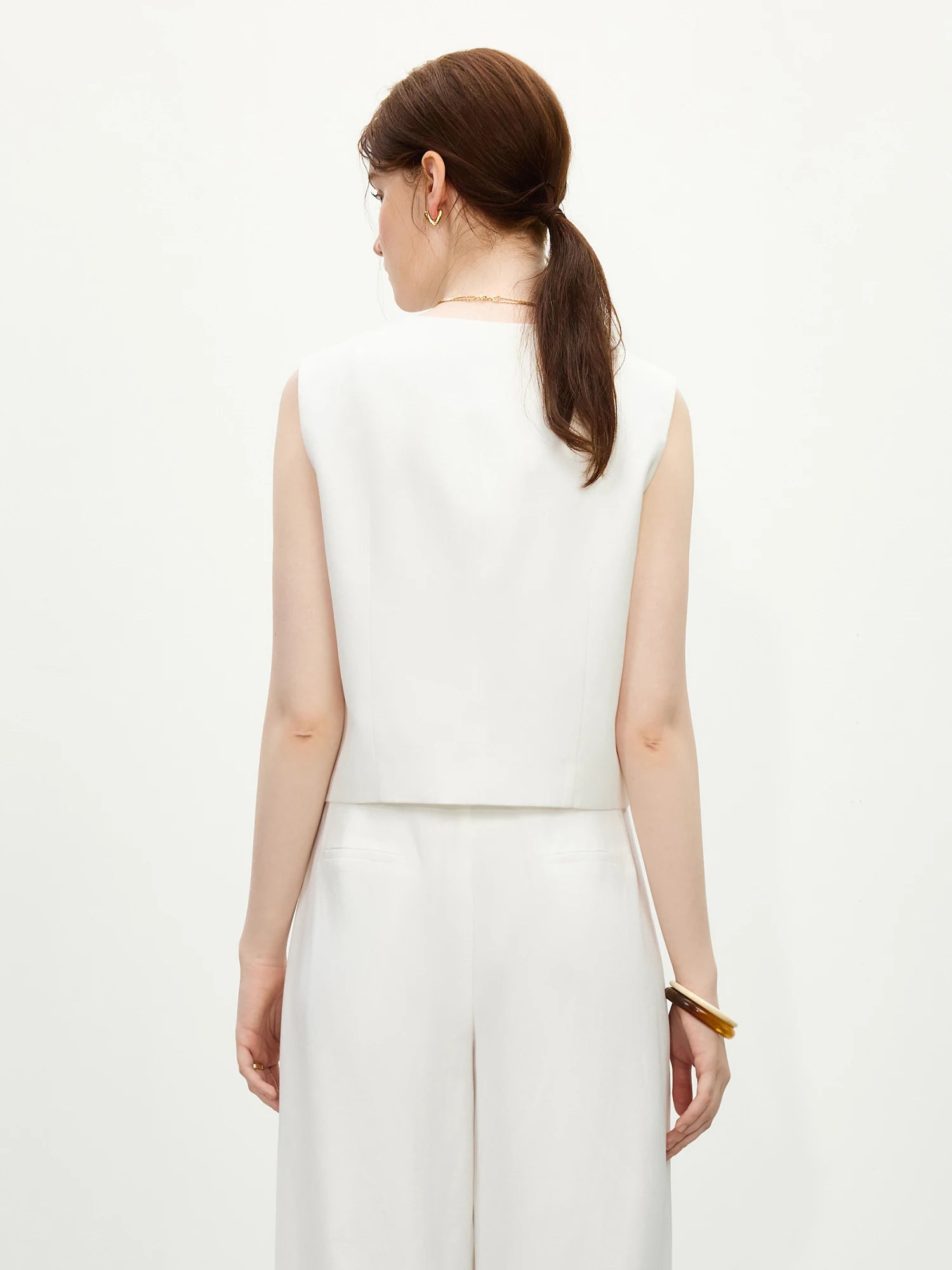 Woman wearing a white sleeveless top and pants on a white background