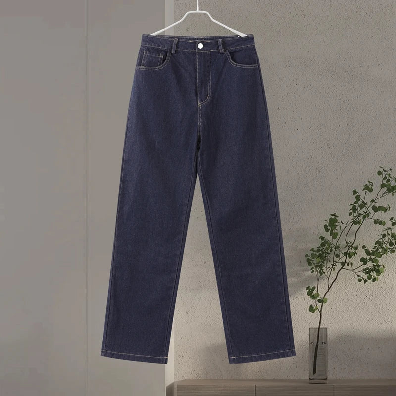 Navy blue jeans hanging on a hanger against a plain wall with a plant in the background.