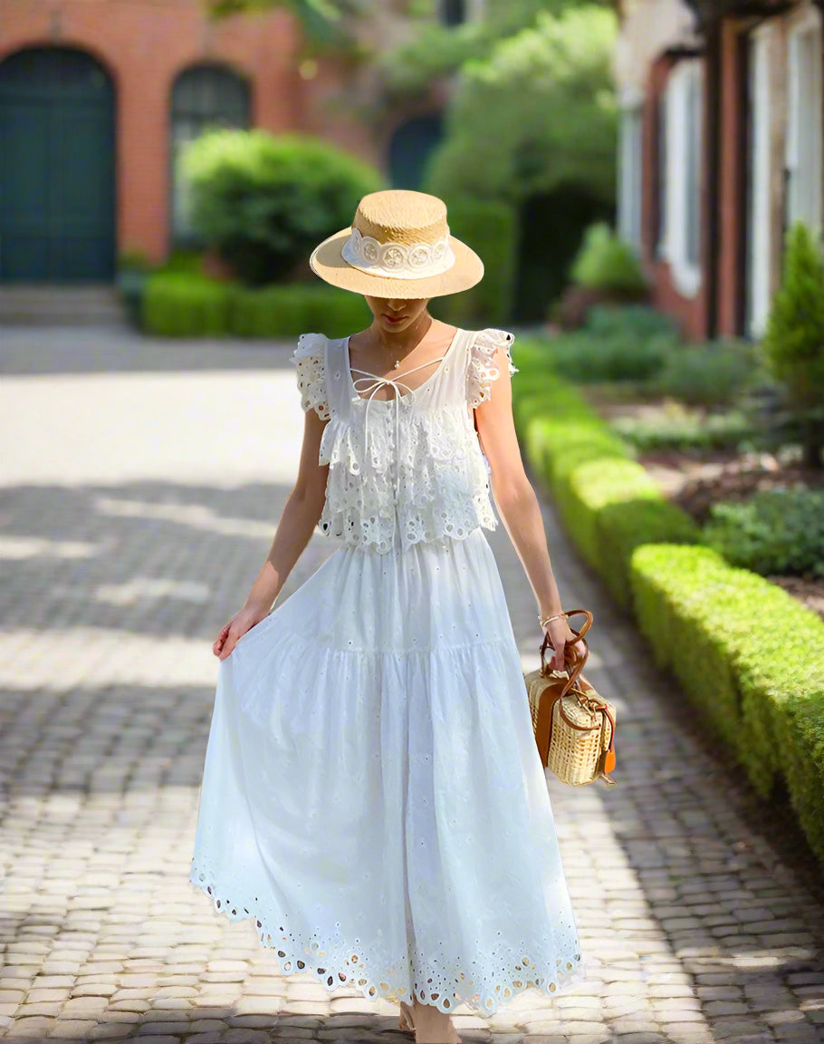 Woman in a white outfit set and straw hat standing in front of a backyard garden, sunny