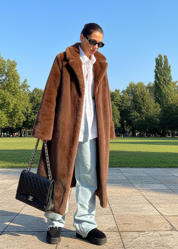 Person wearing a brown fur coat and light blue jeans standing in front of an open park