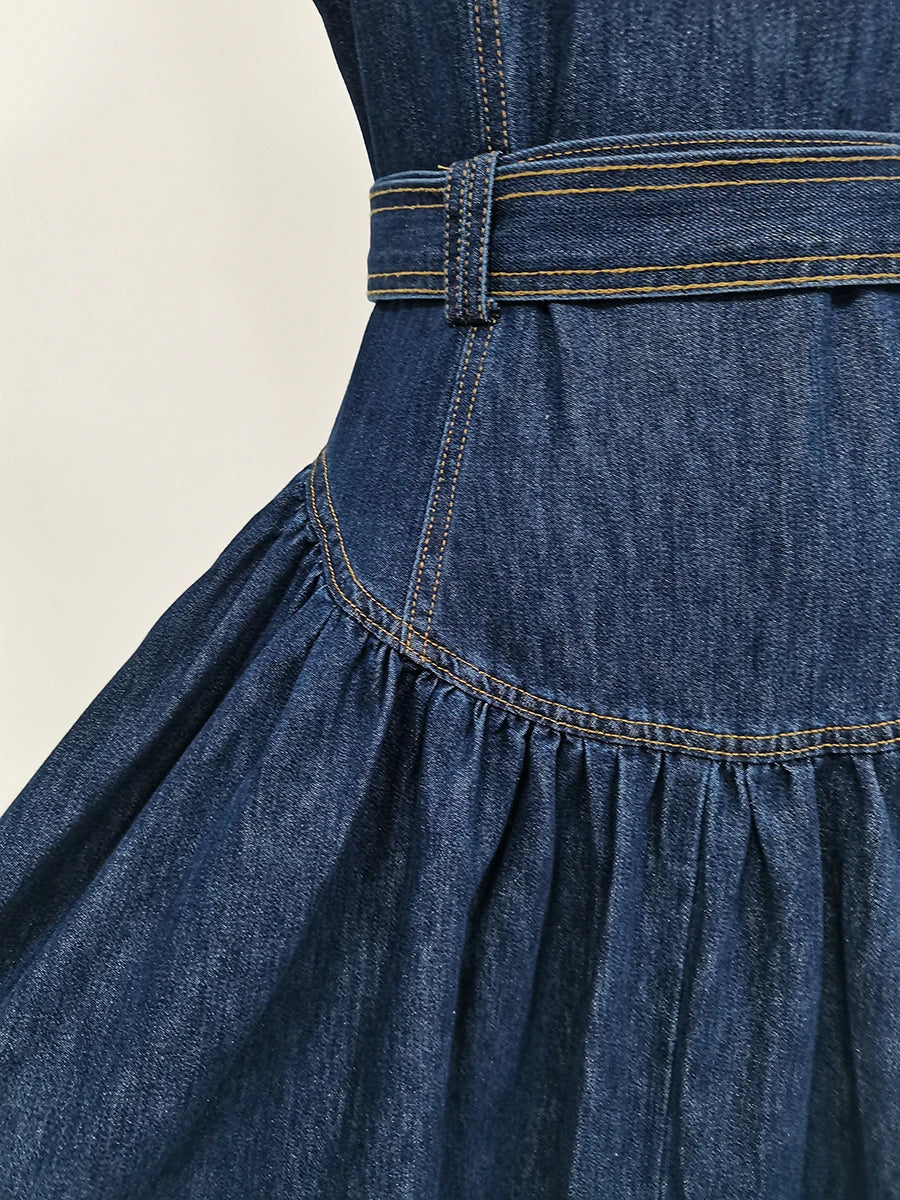 Close-up of a blue denim dress with a belt on a beige background