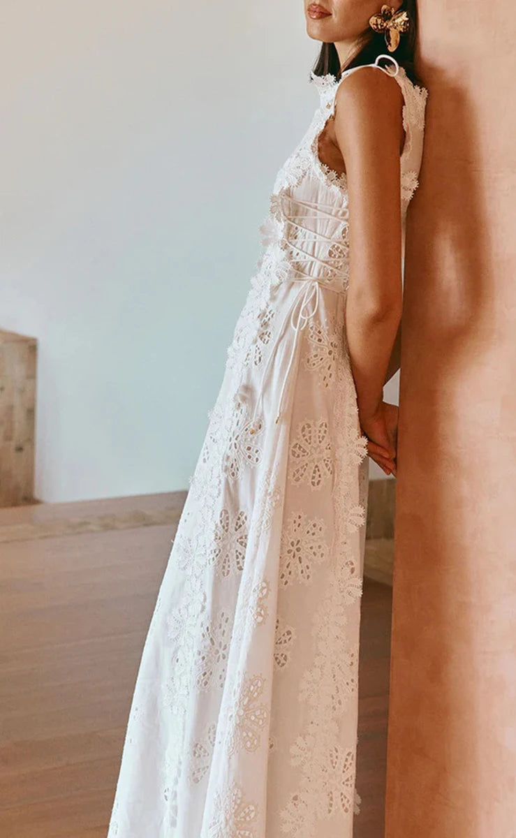 Woman wearing a white lace dress standing against a neutral wall.