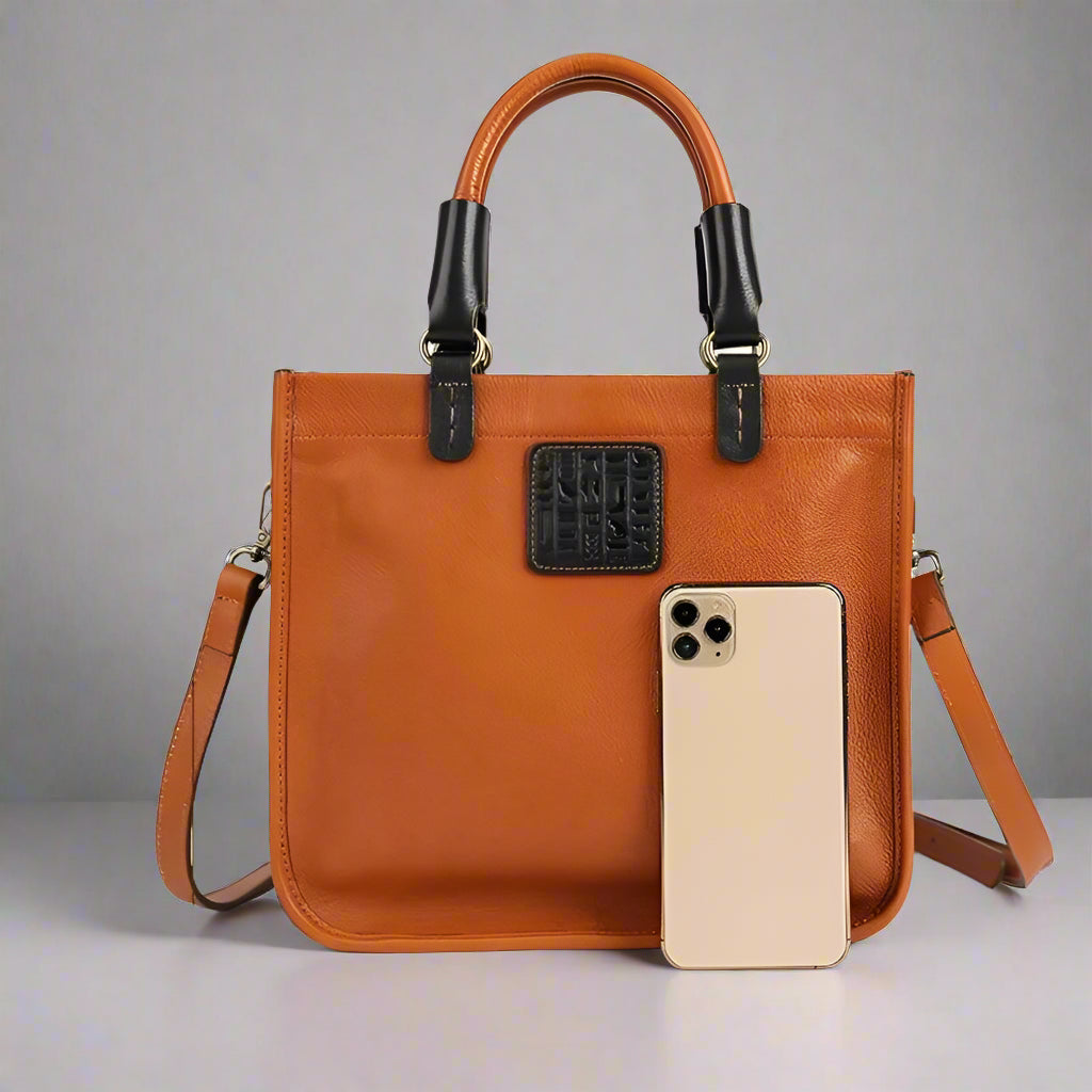 camel color handbag with measurements and a phone for scale on a white background