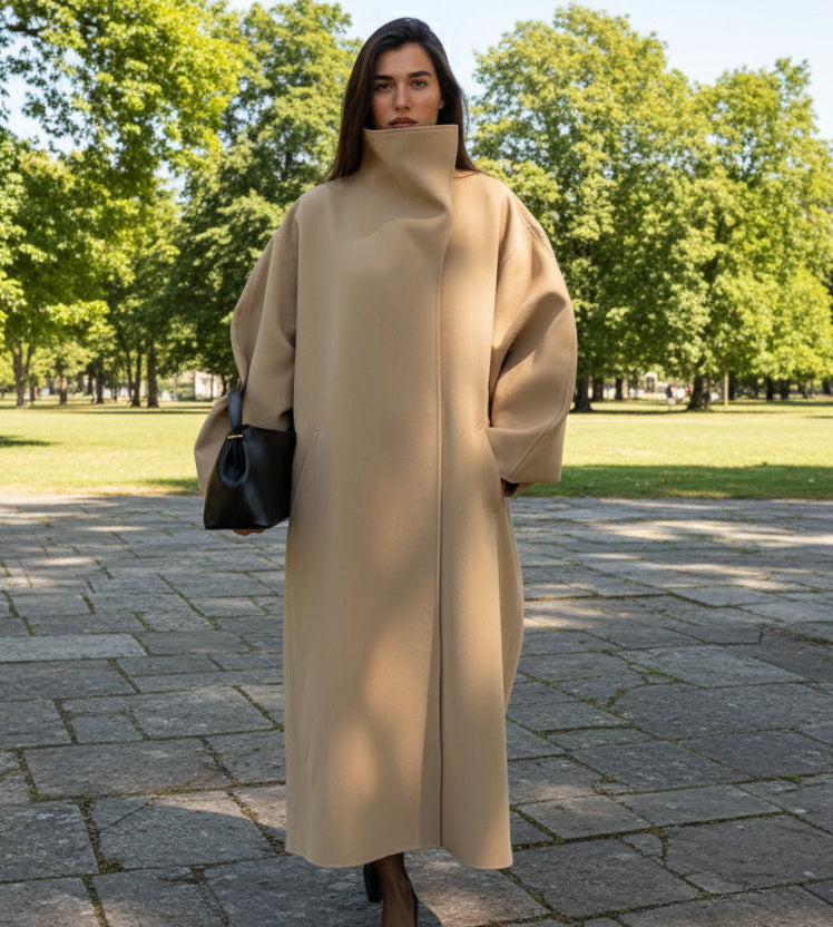 Woman wearing a long beige coat holding a black handbag in an open park