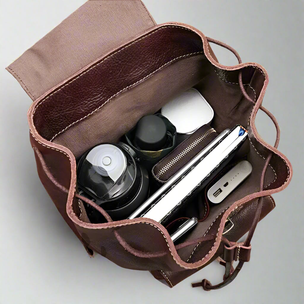 Brown leather bag with compartments containing electronic devices on a white surface