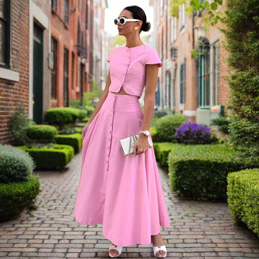 Woman wearing a pink outfit standing against a backyard garden, sunny.