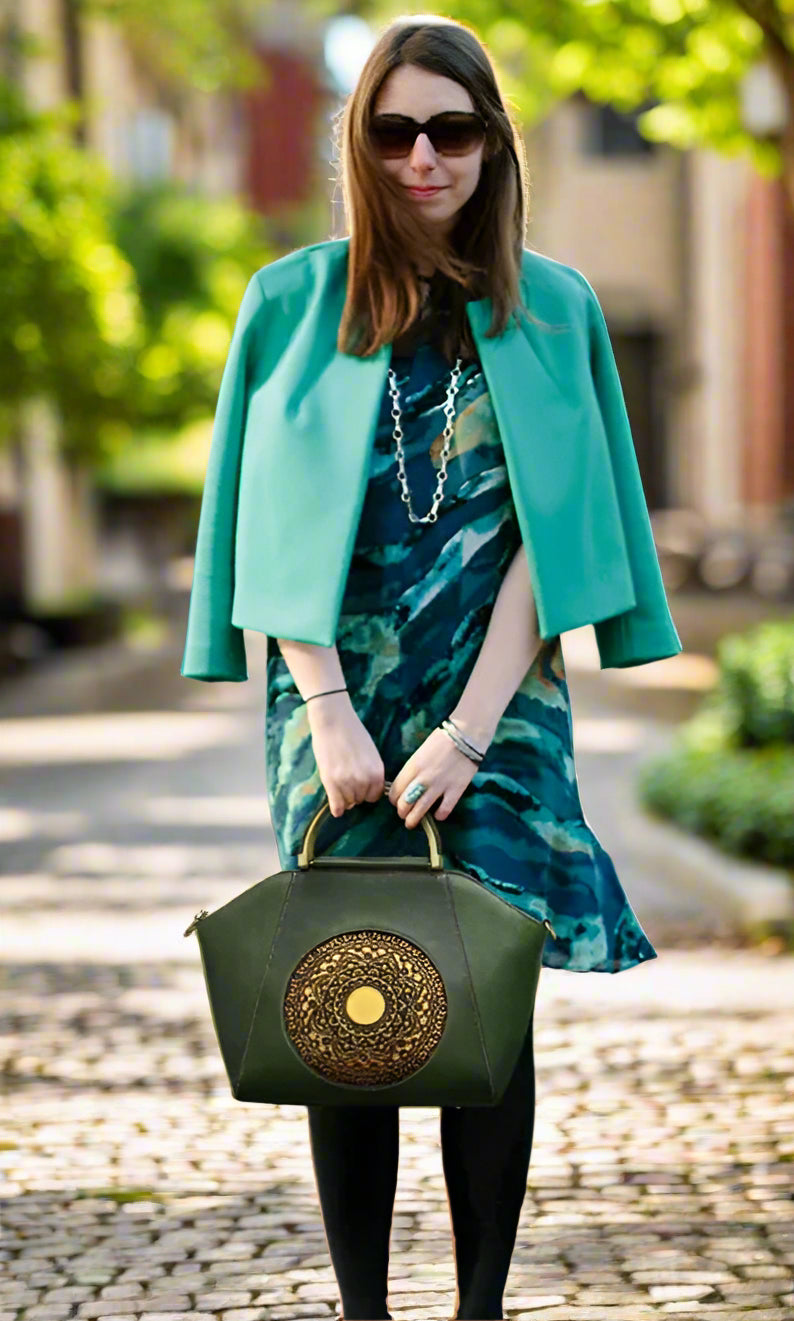 Woman in a green jacket and patterned dress holding a green handbag on a street.
