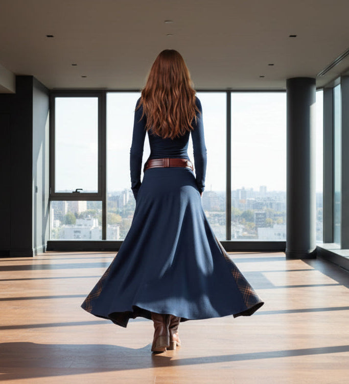 Person wearing a long navy dress with a brown belt and boots against a gray background