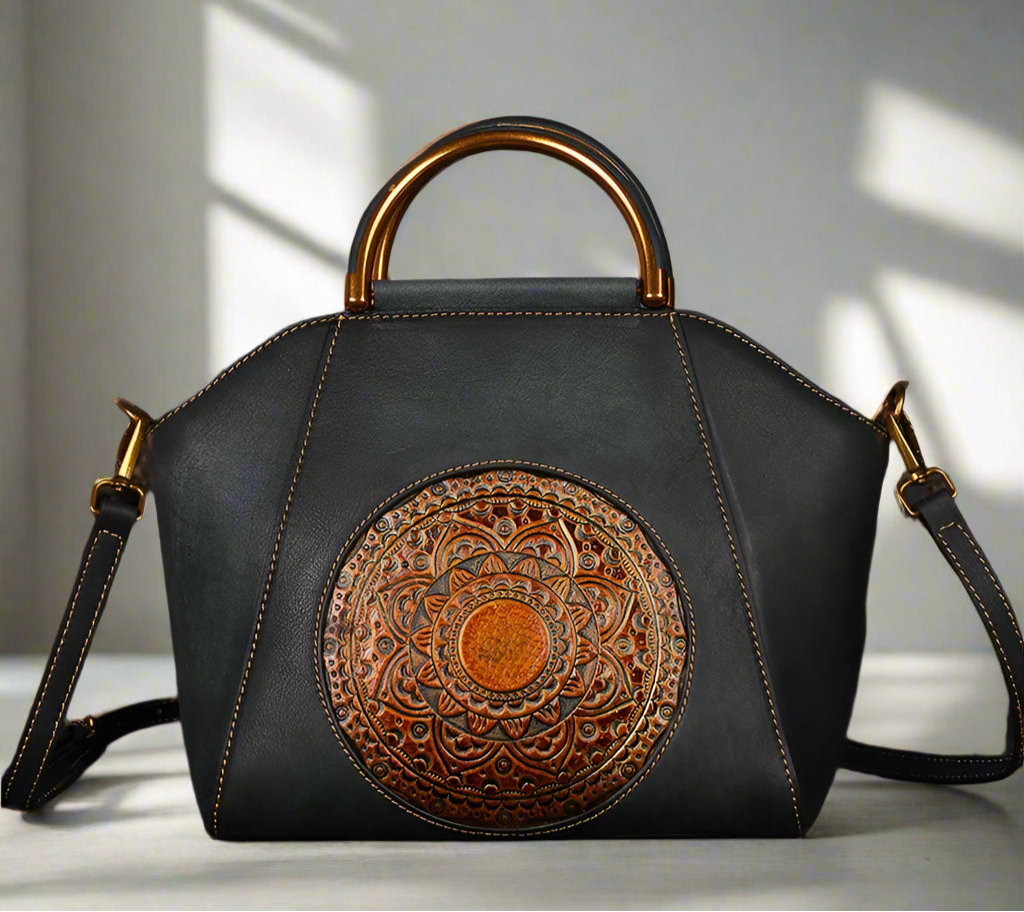 Black leather handbag with gold handle and intricate circular design on a light background