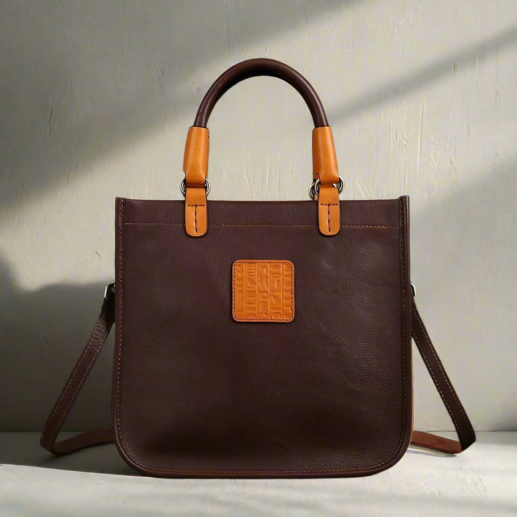 Brown leather handbag with tan handles and accents on a white background