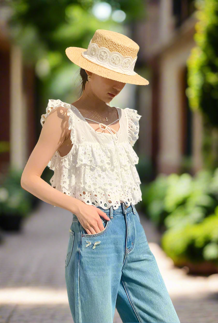 Person wearing a white lace top and blue jeans with a straw hat outdoors.