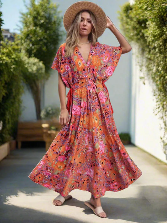 Woman wearing a colorful floral dress and straw hat in an outdoor setting.