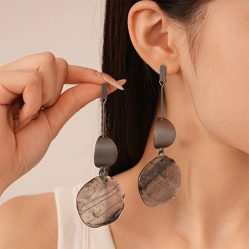 Person wearing a pair of dangling earrings with a neutral background